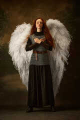 Redhead woman in chainmail and skirt with large white wings and halo looks as angelic warrior...