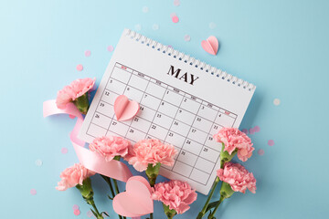 Mother's Day blue serenity: An overhead view of May's calendar, pink carnations, and hearts on a...