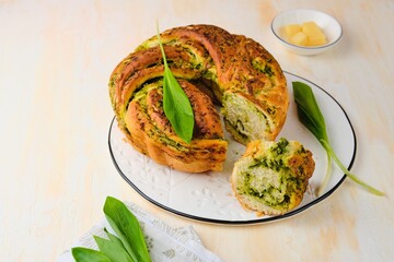 Unsweetened pastries, round snack twisted bread with wild garlic pesto on a white dish on a light concrete background. Ramson recipes.