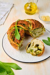 Unsweetened pastries, round snack twisted bread with wild garlic pesto on a white dish on a light concrete background. Ramson recipes.