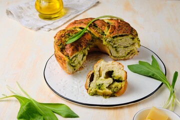 Unsweetened pastries, round snack twisted bread with wild garlic pesto on a white dish on a light concrete background. Ramson recipes.