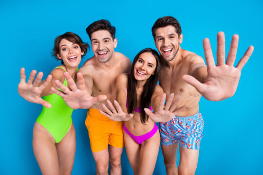Photo of four positive cheerful people dressed swimsuits showing you palms say hello in pool at resort isolated on vivid blue background - Powered by Adobe