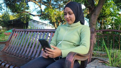 Happy muslim woman listen music on mobile phone at park, using headset, free space