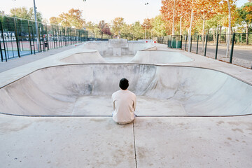 unrecognizable man sitting on a ramp thinking while looking at a vacant skatepark - Powered by Adobe