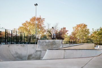 young male skateboarder at the top of an extreme ramp. full view of a skatepark and a man about to...
