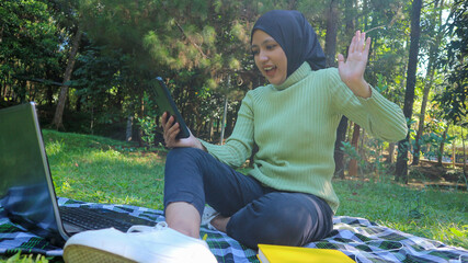 Happy muslim woman having video call on mobile phone at park, using headset, free space