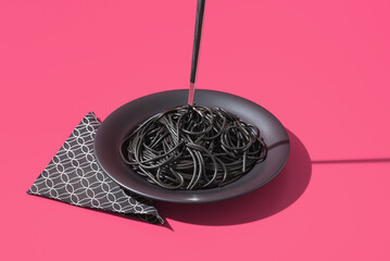 Espaguetis con tinta de calamar negro en un plato con tenedor sobre fondo rosa