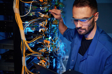 In glasses. Young man is working with internet equipment and wires in server room