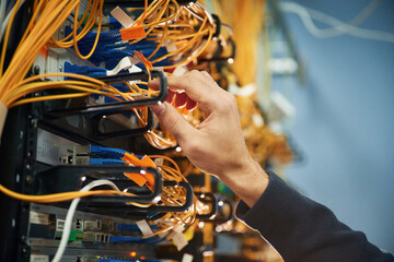 Young man is working with internet equipment and wires in server room