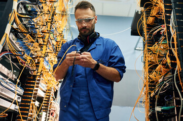 View from below. Young man is working with internet equipment and wires in server room