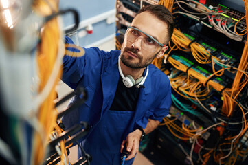 Looking up, management of cables. Young man is working with internet equipment and wires in server...