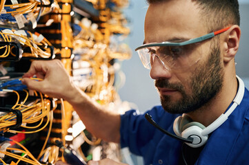 Modern technology routing. Young man is working with internet equipment and wires in server room