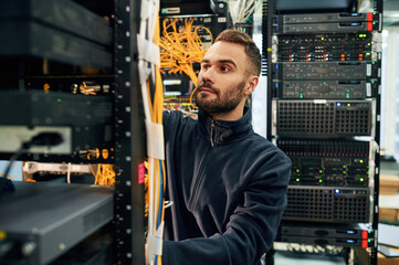 Black clothes. Young man is working with internet equipment and wires in server room