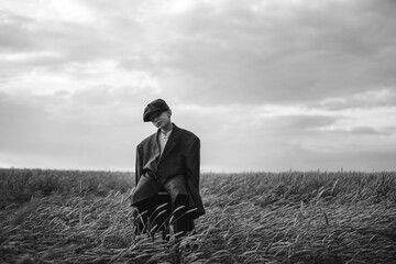 village boy in a cap 9 years old in a wheat field. sits on a chair and looks to the side. black and white photo