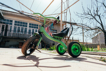 A green tricycle is parked on a sidewalk in front of a house