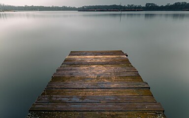 Scene of an empty dock situated in middle of a tranquil body of water, illuminated by a cloudy sky