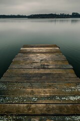 Scene of an empty dock situated in middle of a tranquil body of water, illuminated by a cloudy sky