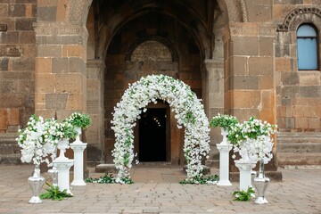 Fototapeta na wymiar a white flower covered arch with plants in large urns