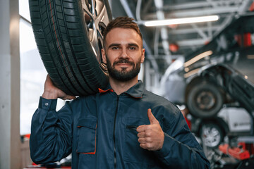 With brand new tire. Car repairman is in the garage with automobile