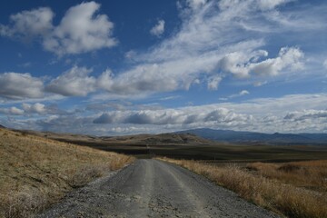Scenic view of a dirt road leading through a lush landscape of grassy hills and mountains