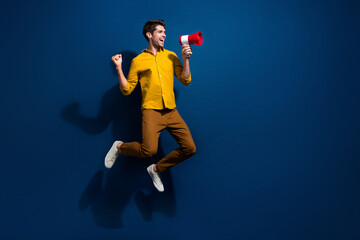 Obraz premium Full body photo of handsome young guy jump scream loudspeaker dressed stylish yellow outfit isolated on dark blue color background