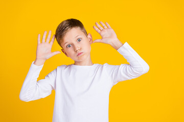 Photo of carefree fooling kid dressed white shirt rising arms palms bloated cheeks empty space isolated yellow color background