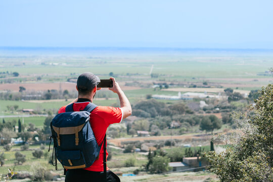 A man is taking a picture of a beautiful landscape with a backpack on his back. Concept of adventure and exploration, as the man is capturing the beauty of nature while on a journey