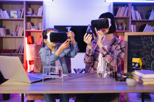 Scientific tests experiments in evening at home for school project ,homework, virtual reality concept. Mother and little daughter girl having fun playing with chemistry lab together using vr glasses.