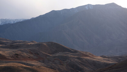 A long winding road through the autumn hills towards the mountains in a blue haze on the horizon.