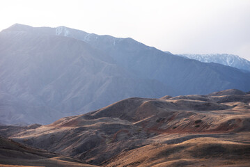 A long winding road through the autumn hills towards the mountains in a blue haze on the horizon.