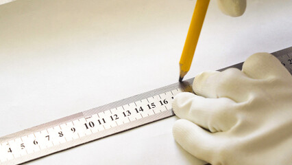 A male construction worker with a metal ruler and pencil draws a line in close-up.