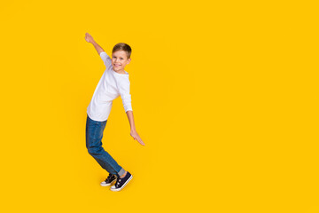 Fototapeta na wymiar Full length photo of good mood funky boy wear white shirt arms sides dancing empty space isolated yellow color background