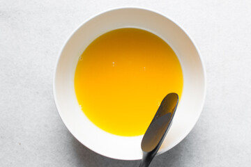 overhead view of melted butter in a white ceramic mixing bowl, top view of melted butter in white...