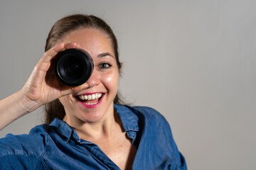 Mujer mirando a través de lente de cámara fotográfica haciendo un gesto de sorpresa y asombro - obrazy, fototapety, plakaty