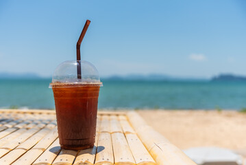 Ice black coffee and sea beach background, iced coffee americano in take away cup on the beach.