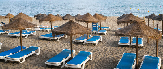 Beach resort, sea summer vacation concept. Lounge wooden sunbeds with umbrellas. A row of sunbeds...