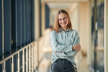 Smiling, standing with arms crossed, in glasses. Young woman in airport hall