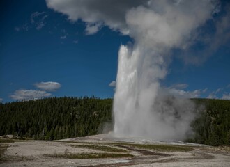 Scenic view of a geyser against a mountain covered with green forest