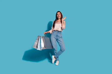 Full length photo of impressed girl wear silk blouse jeans hold shopping bags look at sale empty space isolated on blue color background
