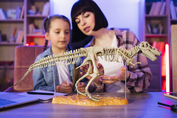 Two female sitting together at table and make model of tyrannosaurus out of bones at evening time...