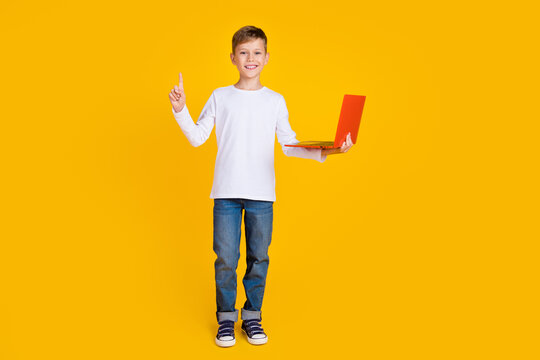 Full length photo of sweet excited kid dressed white shirt pointing finger studying modern device isolated yellow color background