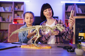 Happy mother examine skeleton of dinosaur with smart cute daughter recording content for natural...