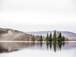 a lake with trees on the side and hills in the background