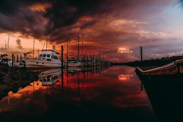 Ominous landscape featuring multiple boats, illuminated by the orange hues of the sunset