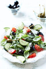 Salad with black Olives, cherry Tomatoes, Cucumber and Rocket on bright Background. Close up.