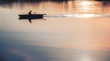 Silhouette of a person paddling a canoe in a river as the sun begins to set