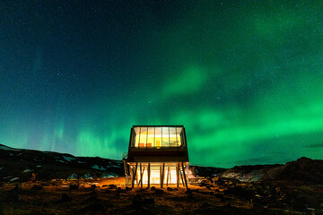 Aurora borealis, Northern lights glowing over luxury hotel on volcanic wilderness in winter at...