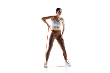 Muscular woman in workout pose with resistance band against white studio background, Strength and...