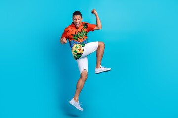 Fototapeta na wymiar Full body photo of nice young man jump raise fists empty space summer holiday isolated on blue color background