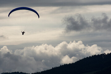 Silhouette of a man paragliding over a mountain on a cloudy day.